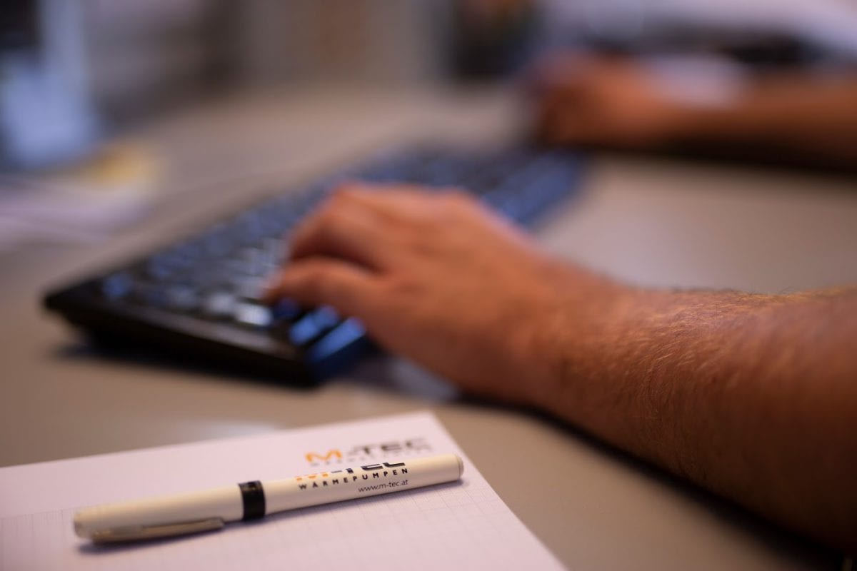 eine Person, die auf der Tastatur tippt und neben der ein Stift und Papier liegt