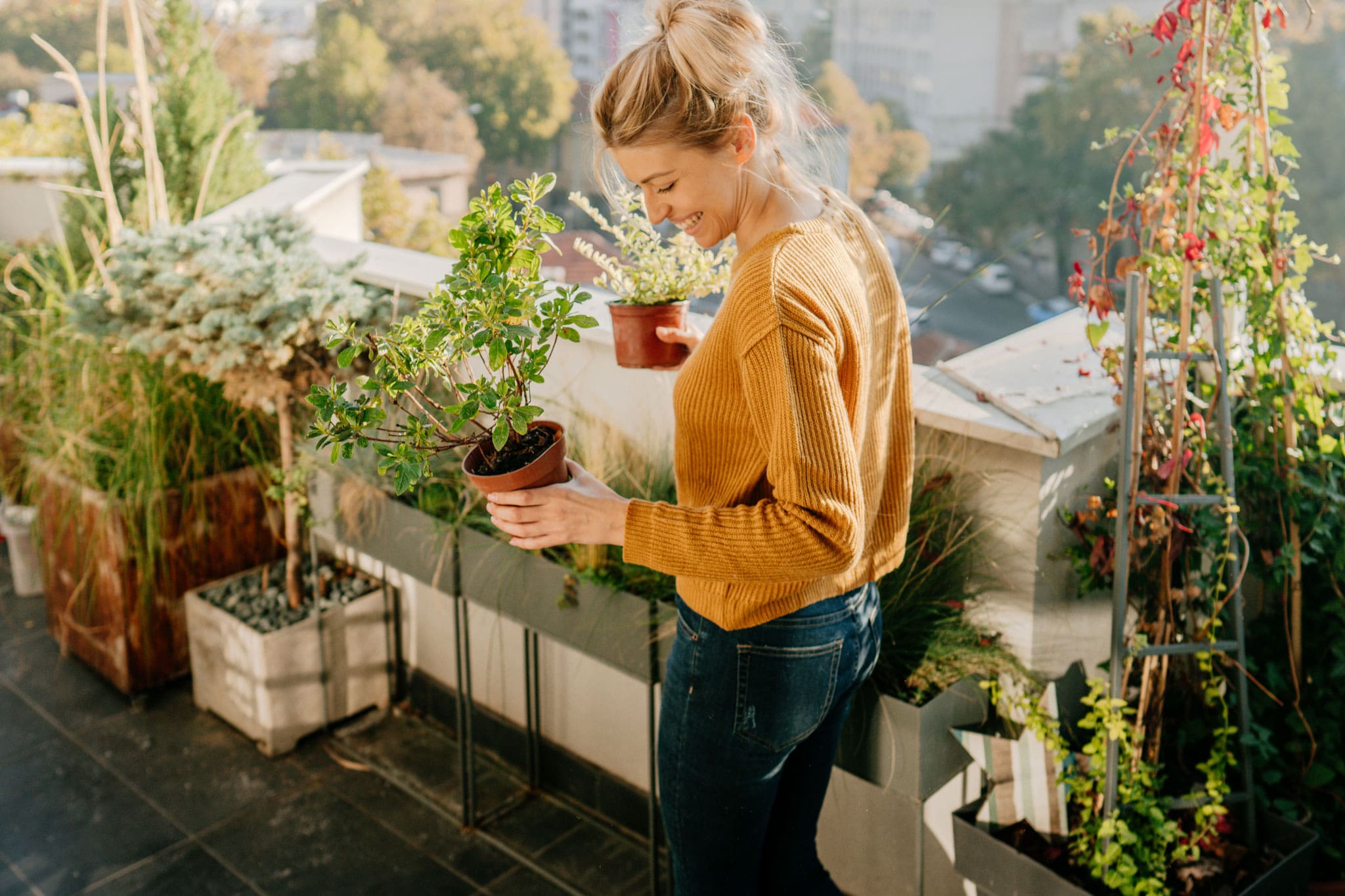 eine Frau steht in einem Bereich mit Pflanzen und Blumen. Sie hält zwei kleine Vasen und sieht glücklich aus